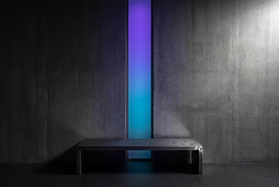A vertical band of light shifting from purple to teal in front of a concrete wall